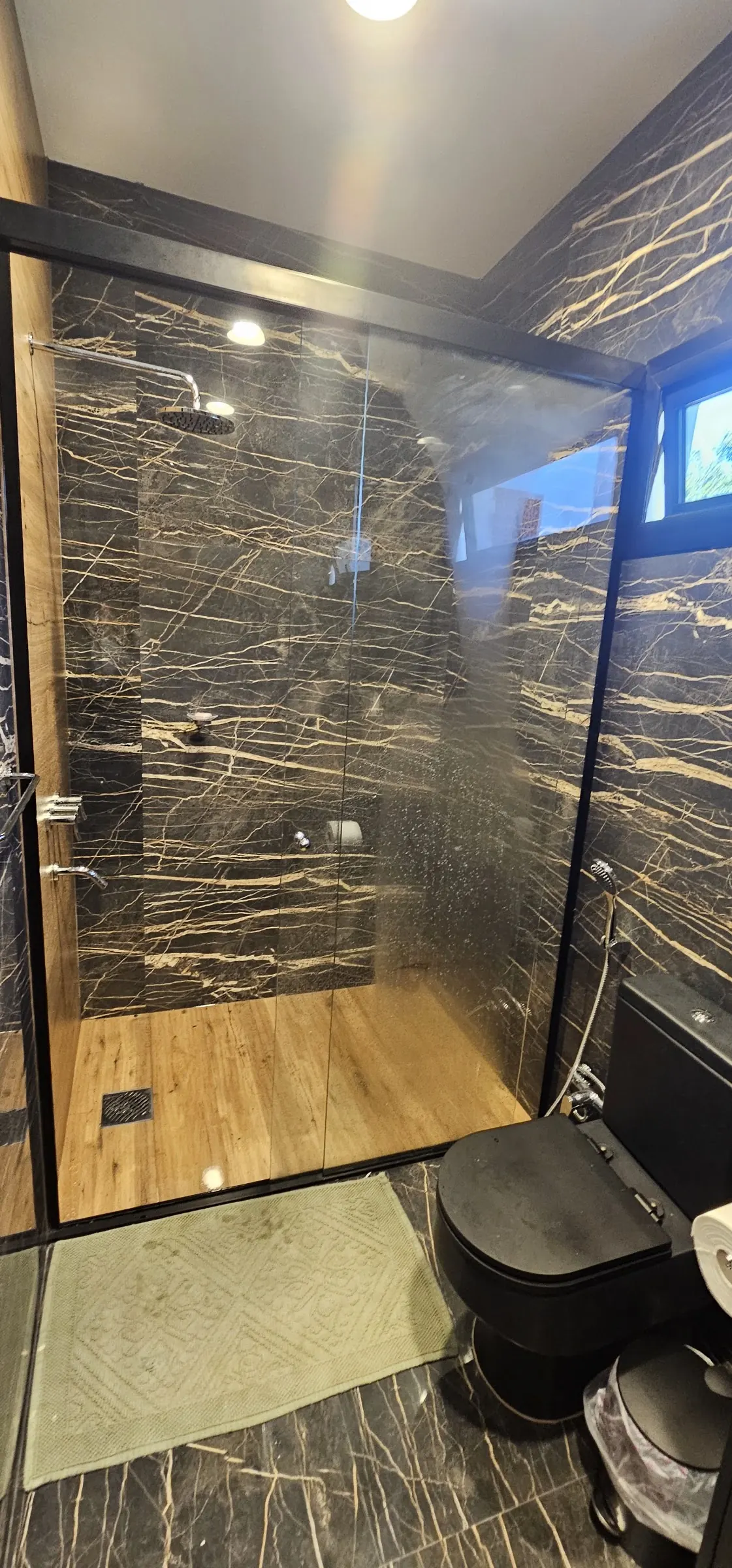 Baño con revestimiento negro y mampara de vidrio